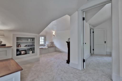 Discover your new favorite retreat! This cozy reading area features custom built-in shelving and a sun-drenched window seat, all tucked under charming sloped ceilings for a true sanctuary feel.