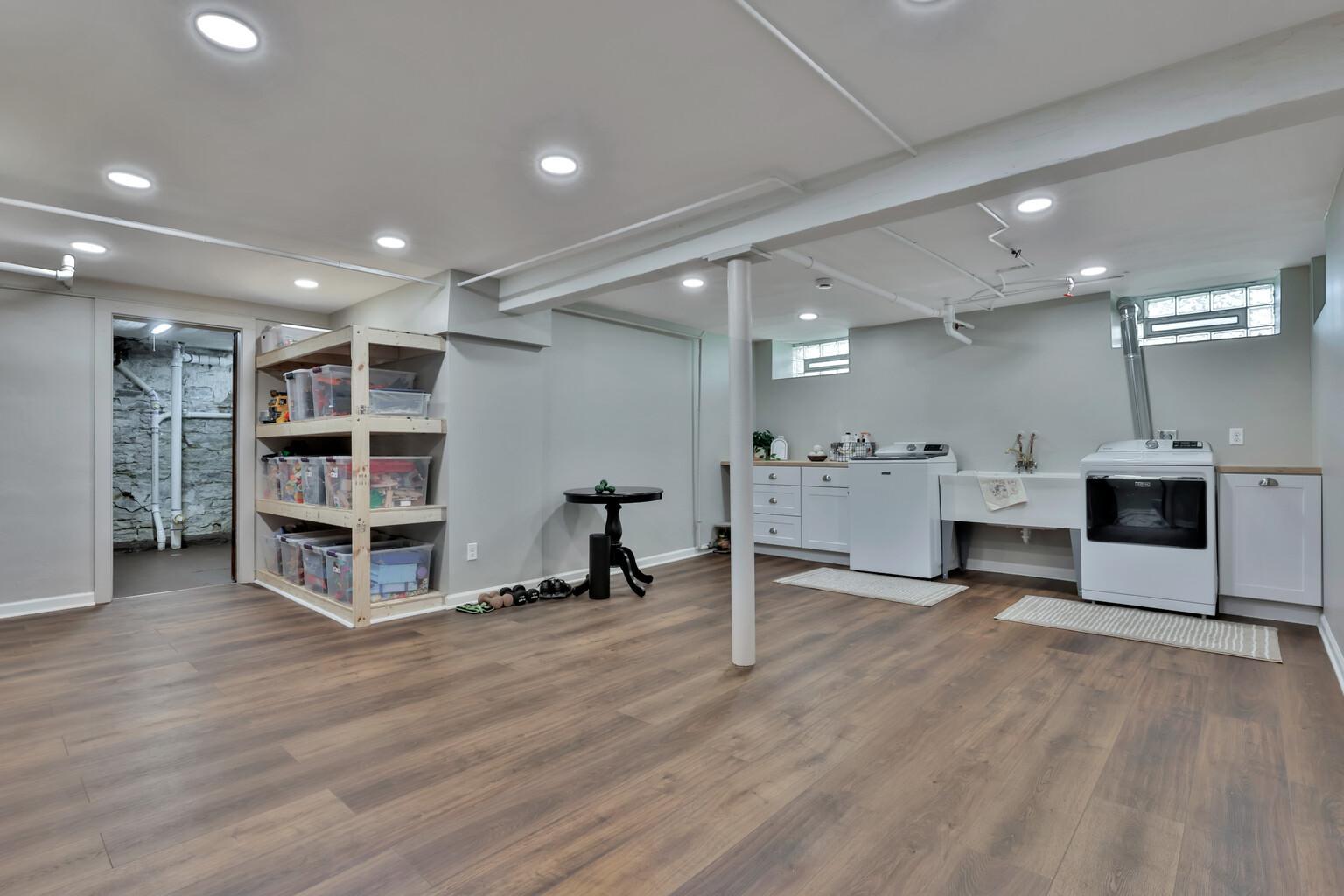 Bright, finished lower level featuring a spacious laundry suite. Boasts custom white cabinetry, ample counter space, and durable wood-look flooring. A clean, organized area with plenty of storage.