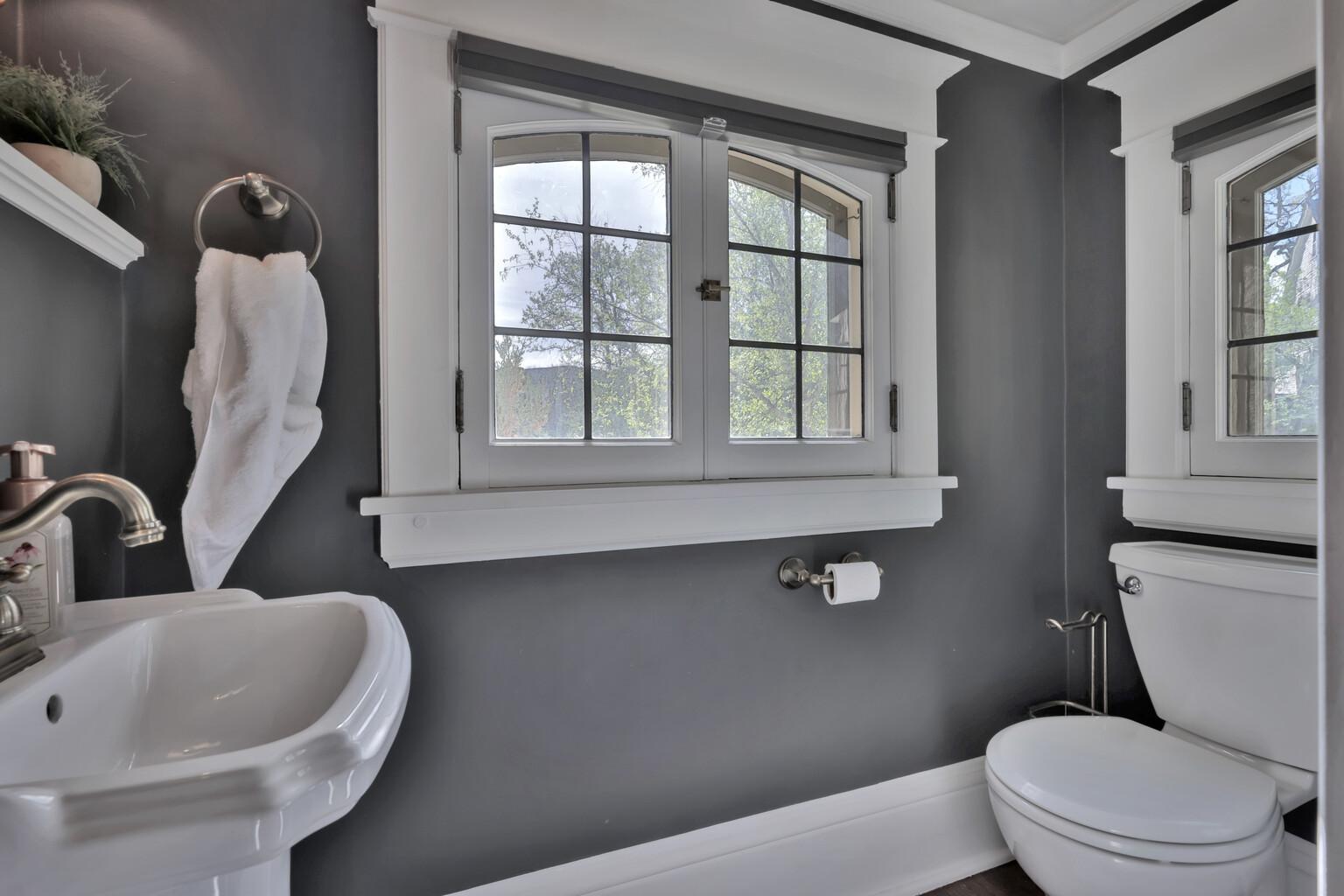 Newly added main-floor half bath featuring cozy heated floors and a classic pedestal sink. Designer charcoal walls, elegant sconce lighting, and timeless millwork create a chic, polished powder room for your guests.