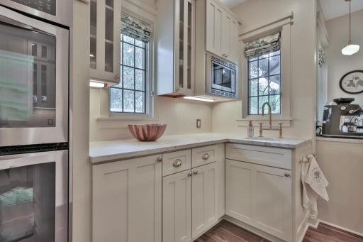 Stunning kitchen boasting leathered natural stone, professional enameled cabinets, & brass hardware. Includes a farmhouse sink, bar prep area with chiller, & tile backsplash over heated wood-look ceramic floors.