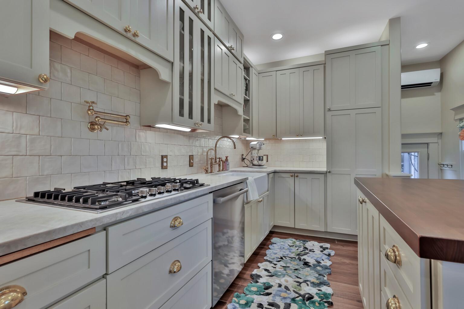 Stunning kitchen boasting leathered natural stone, professional enameled cabinets, & brass hardware. Includes a farmhouse sink, bar prep area with chiller, & tile backsplash over heated wood-look ceramic floors.