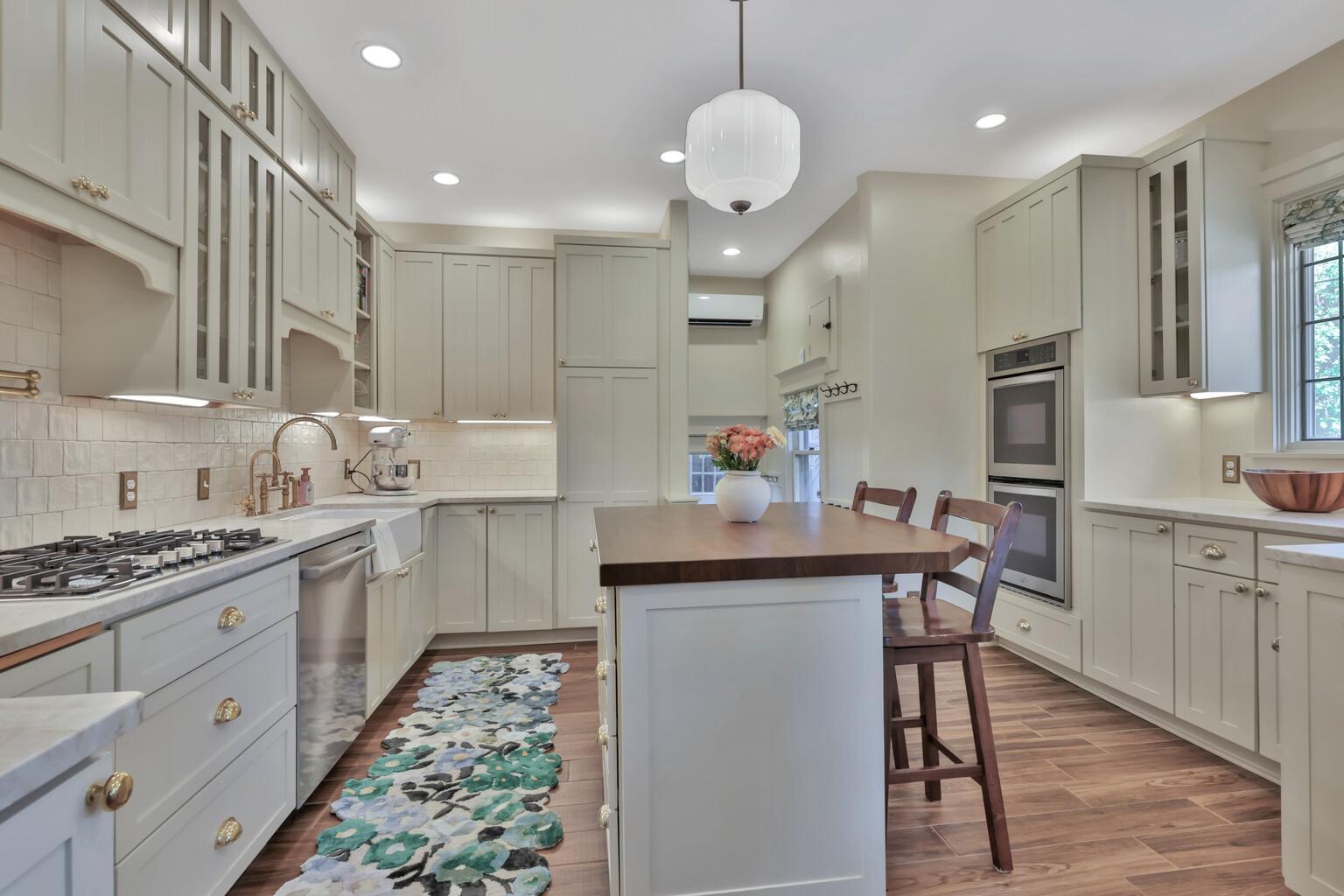 Stunning kitchen boasting leathered natural stone, professional enameled cabinets, & brass hardware. Includes a farmhouse sink, bar prep area with chiller, & tile backsplash over heated wood-look ceramic floors.