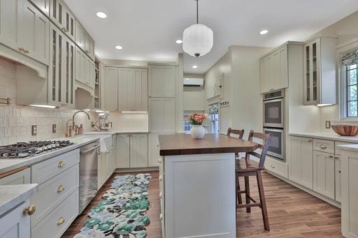 Stunning kitchen boasting leathered natural stone, professional enameled cabinets, & brass hardware. Includes a farmhouse sink, bar prep area with chiller, & tile backsplash over heated wood-look ceramic floors.