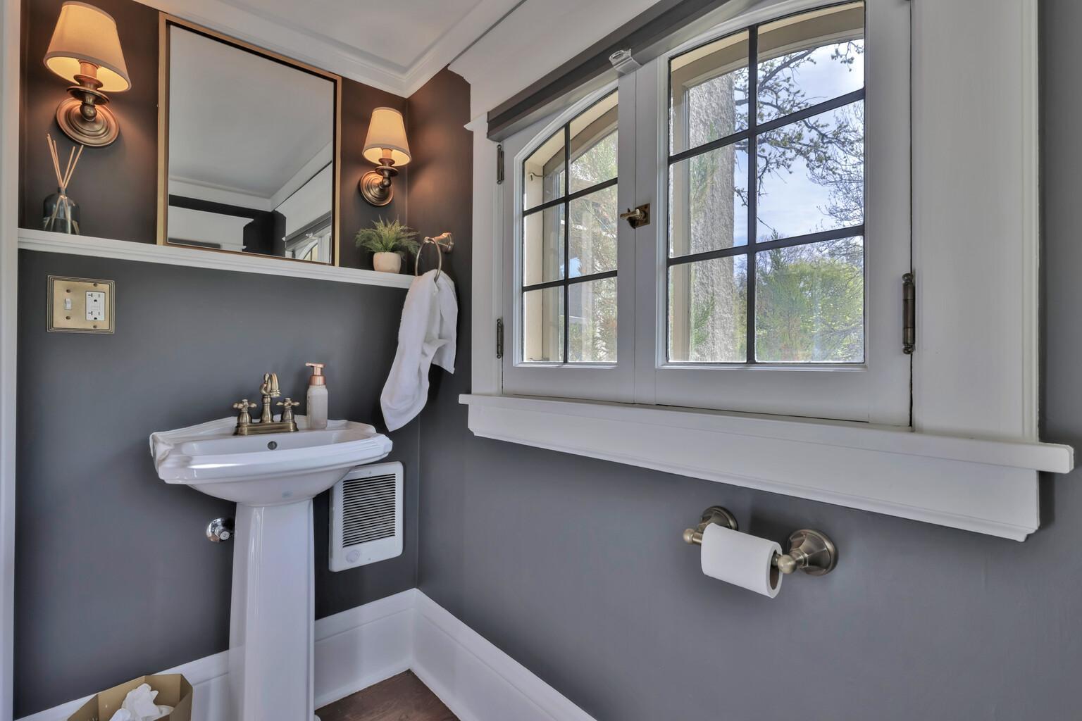 Newly added main-floor half bath featuring a classic pedestal sink, designer charcoal walls, elegant sconce lighting, and timeless millwork create a chic, polished powder room for your guests.