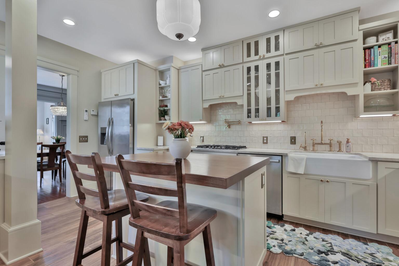 Stunning kitchen boasting leathered natural stone, professional enameled cabinets, & brass hardware. Includes a farmhouse sink, bar prep area with chiller, & tile backsplash over heated wood-look ceramic floors.