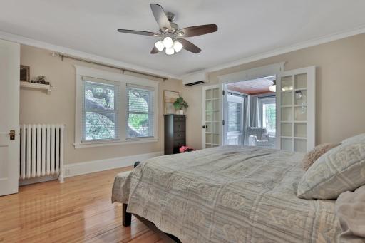 Spacious primary suite featuring polished hardwoods and elegant French doors that open to a sun-drenched sunroom. A private, peaceful retreat with natural wood ceilings and panoramic views.