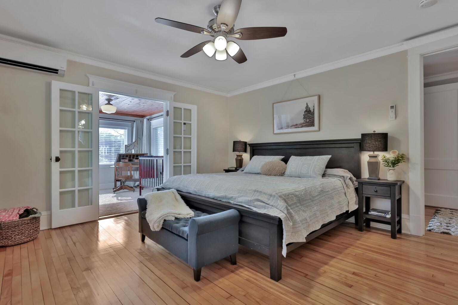 Spacious primary suite featuring polished hardwoods and elegant French doors that open to a sun-drenched sunroom. A private, peaceful retreat with natural wood ceilings and panoramic views.
