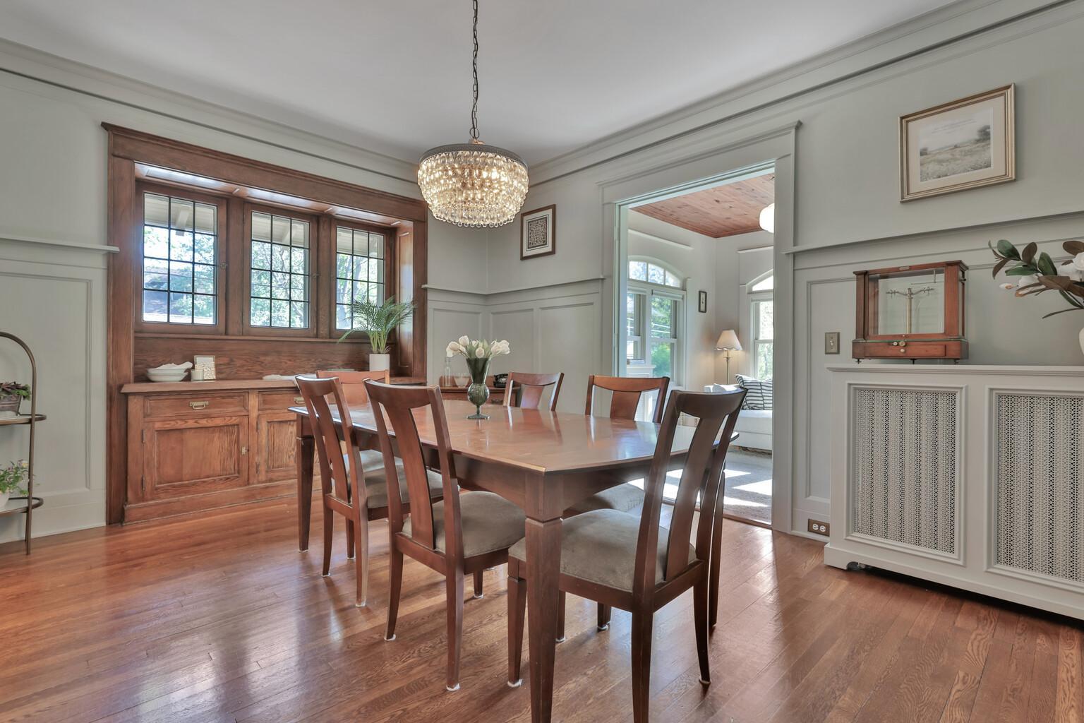 Grand dining room with a custom built-in buffet, classic plate rail, and gleaming hardwoods. Large windows and intricate woodwork create a stately setting.