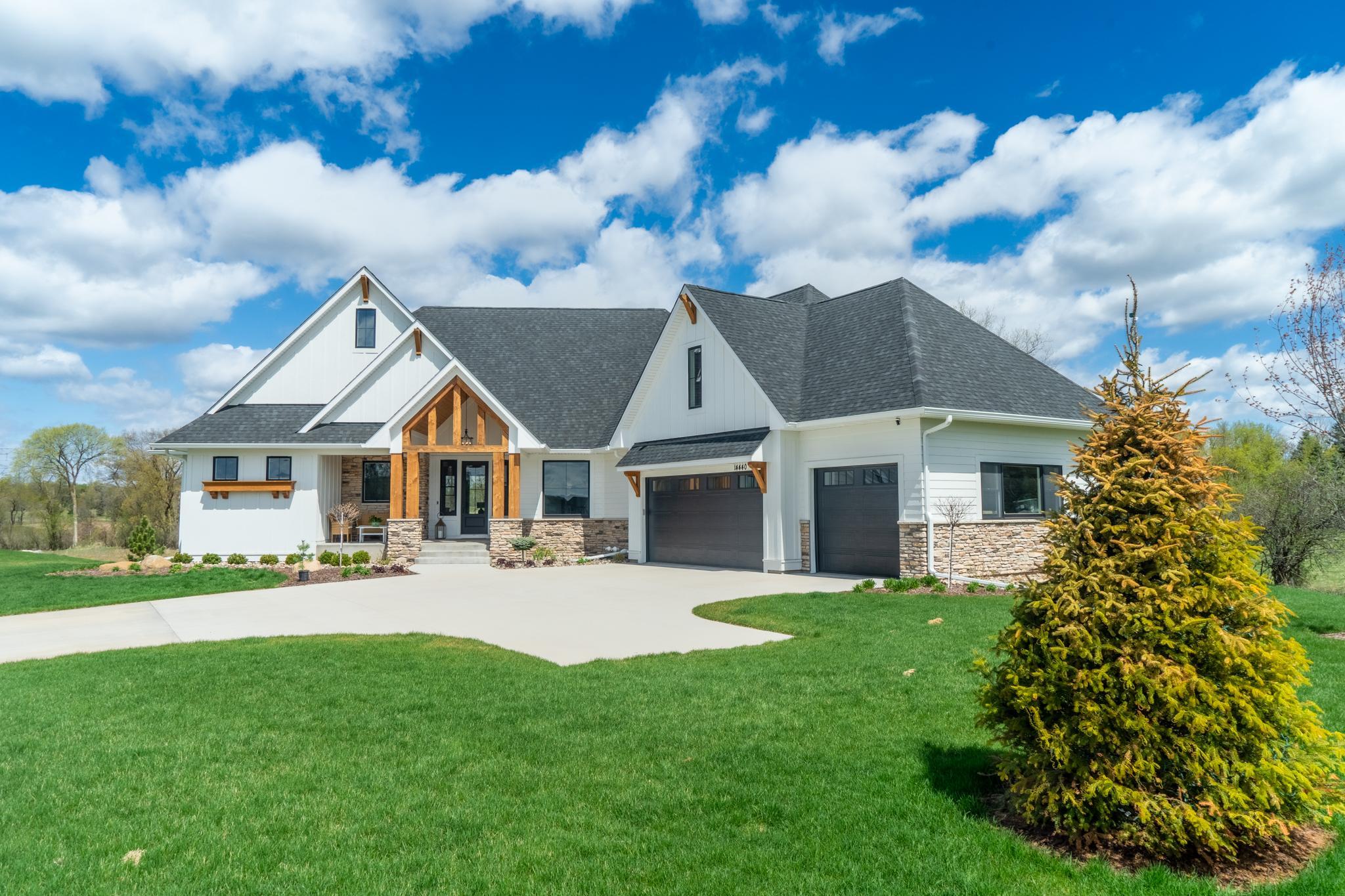 A stunning modern farmhouse with cedar timber accents, stone foundation, and a sweeping green lawn that makes every arrival feel like coming home.