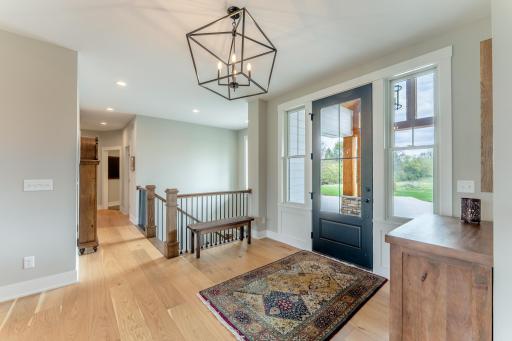Step through the bold black entry door into a light-filled foyer where wide-plank hardwood floors and an artisan geometric chandelier set the tone for everything that follows.
