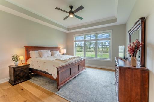 A tranquil primary suite with a tray ceiling, ceiling fan, rich hardwood furniture tones, and sweeping nature views that make waking up feel like a getaway.