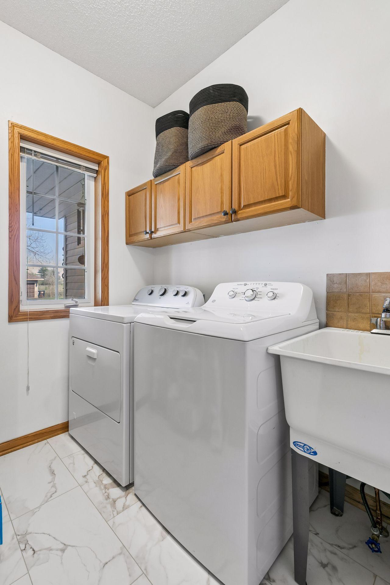 Functional laundry room with utility sink, upper cabinetry, and natural light. Plus, new flooring has just been installed.