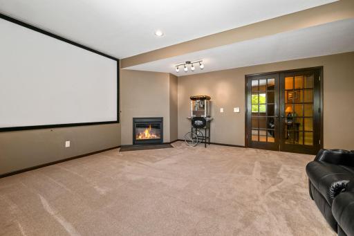 Alternate view of theater room shows fireplace and french doors leading to stairway.