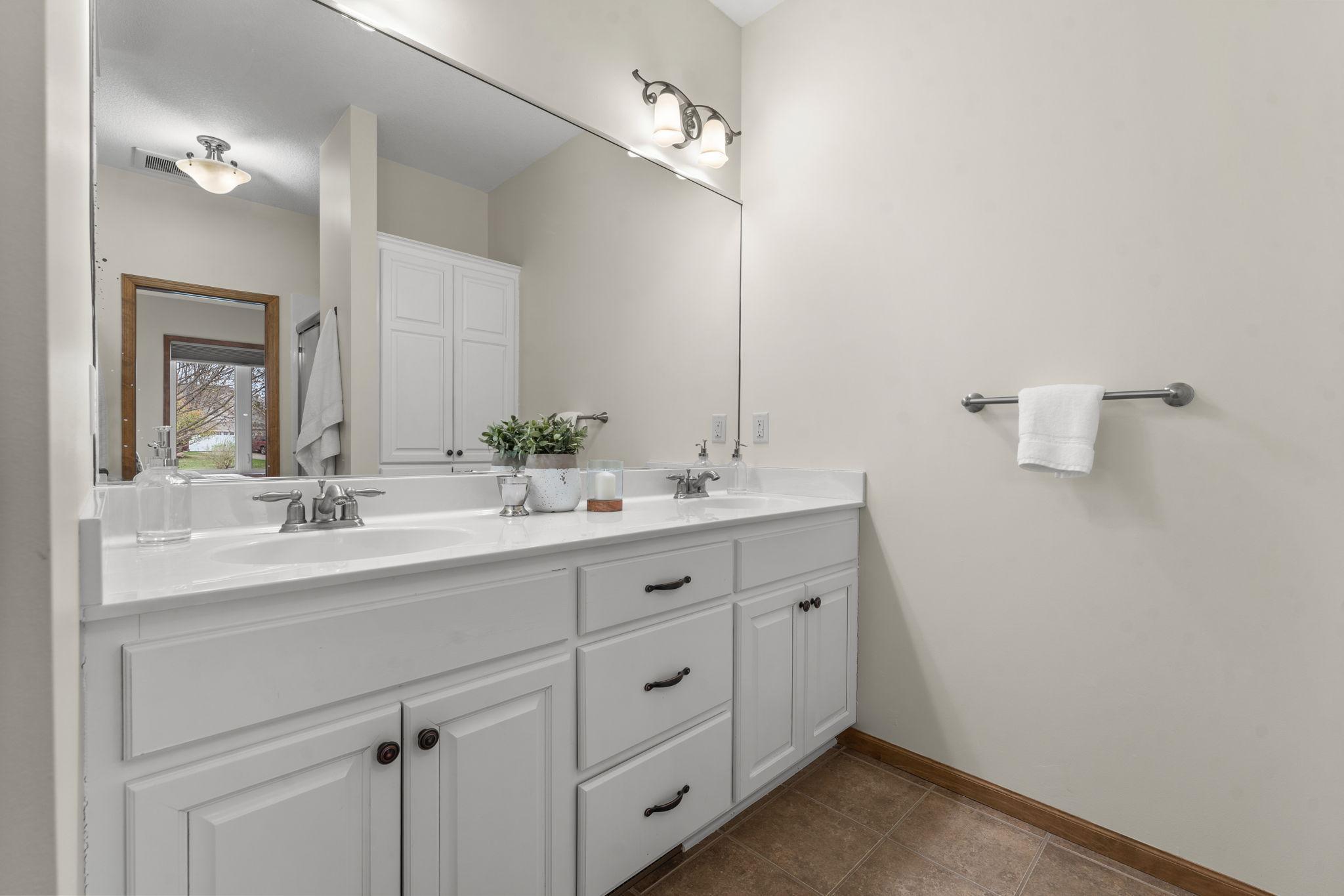 The private ensuite bathroom featuring tile floors, a spa-like soaking tub, walk-in shower, and dual vanities.
