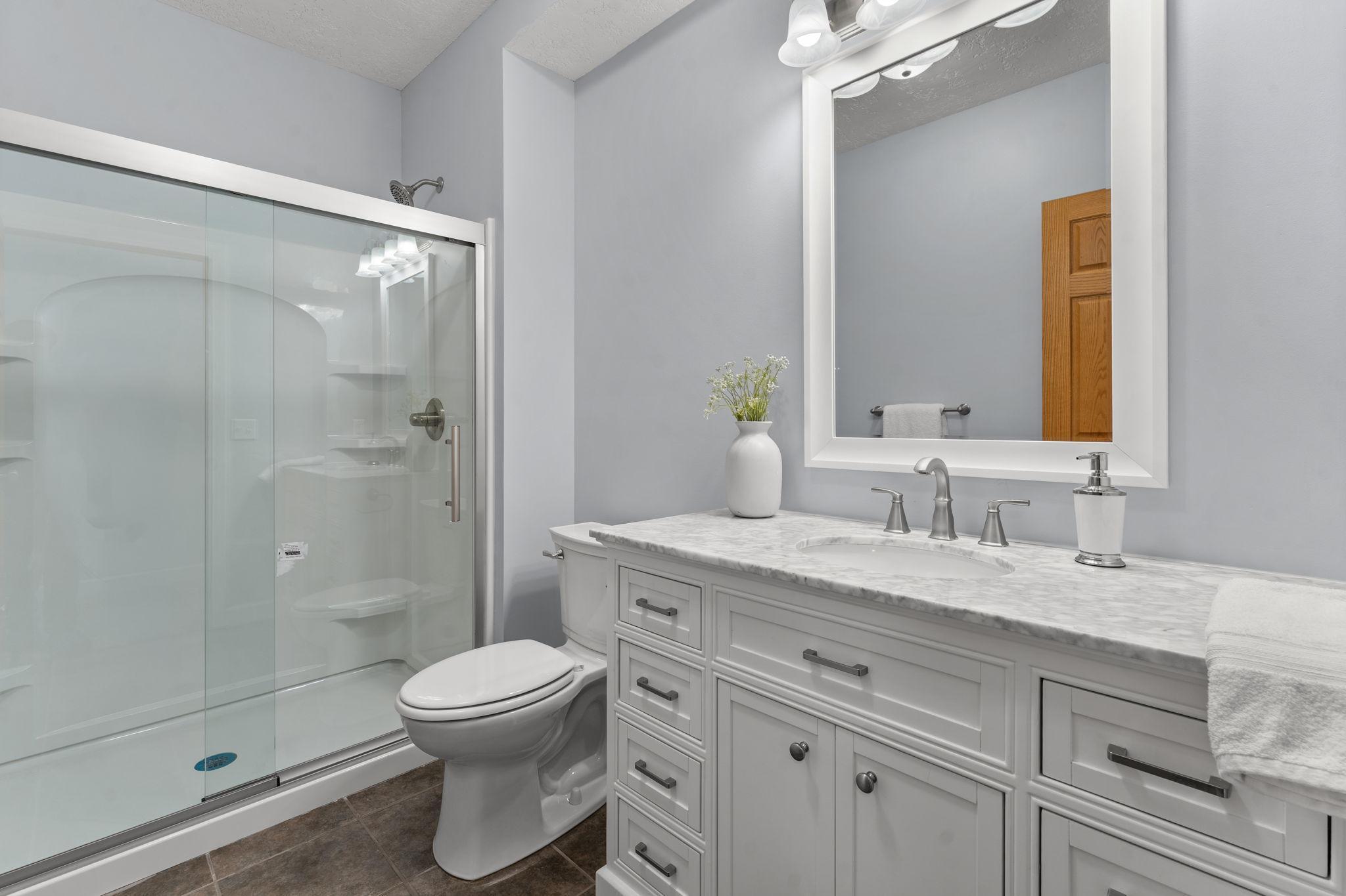 Just steps away is a shared ¾ bathroom with tile floors, a single vanity, and walk-in shower.