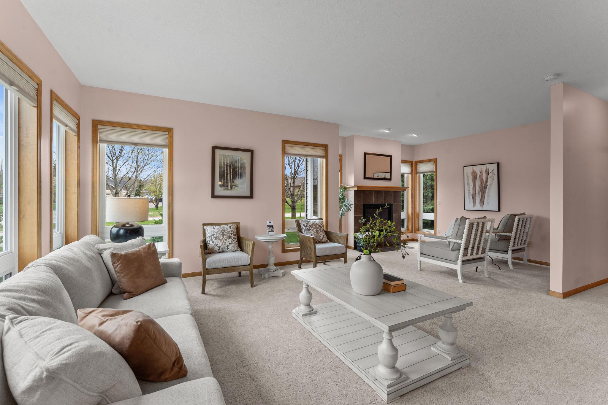 A bright and welcoming space with surrounding windows, soft carpeting, and a cozy gas fireplace with tile surround and wood mantel.