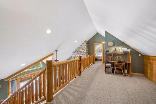 Cozy loft showcasing the beautiful hand carved railing overlooking the main level living room. Ideal space for more room to gather, hang out, work or simply relax. Extra built-in storage along wall is ideal to help stay organized.