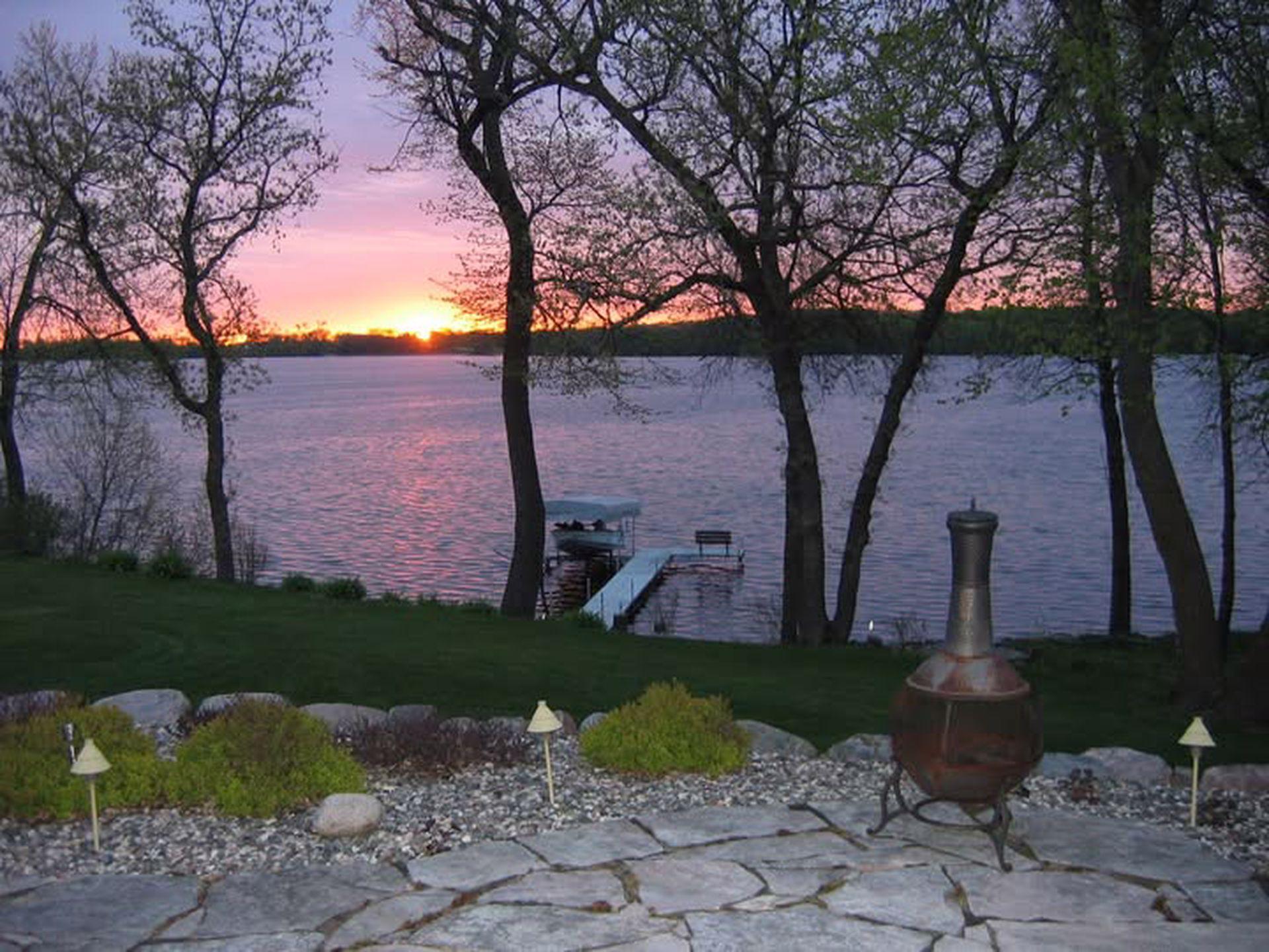 Peaceful lakeside sunrise view framed by mature trees. Enjoy your private dock, calm waters, and flagstone patio. Perfect way to start your day with a cup of coffee enjoying the beauty of lakefront living.