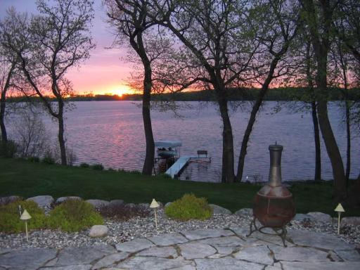 Peaceful lakeside sunrise view framed by mature trees. Enjoy your private dock, calm waters, and flagstone patio. Perfect way to start your day with a cup of coffee enjoying the beauty of lakefront living.