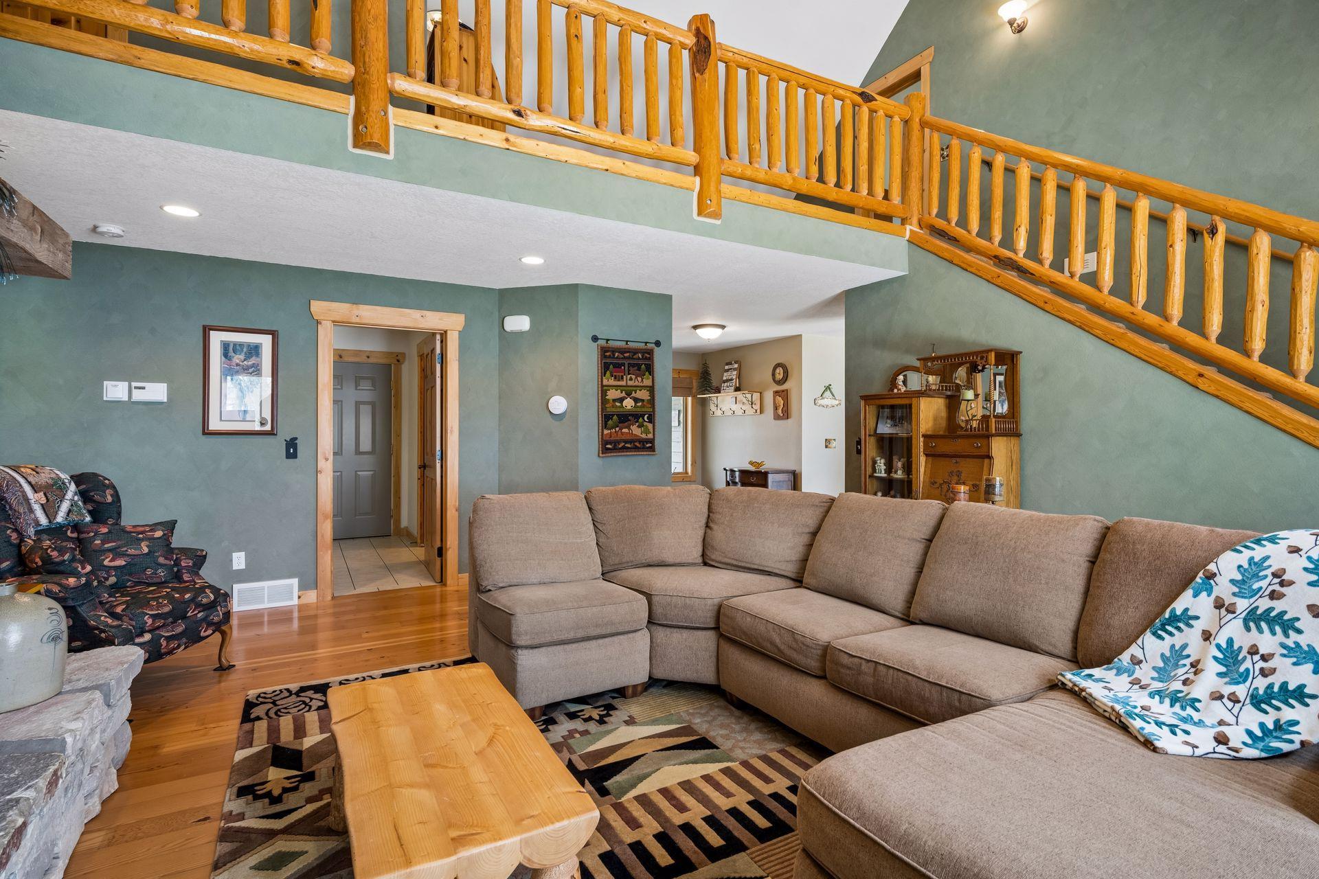 Hand carved custom pine log railings show upper loft area and cozy gathering space for more guests. Open layout and soft light create a welcoming retreat to relaxing in comfort.