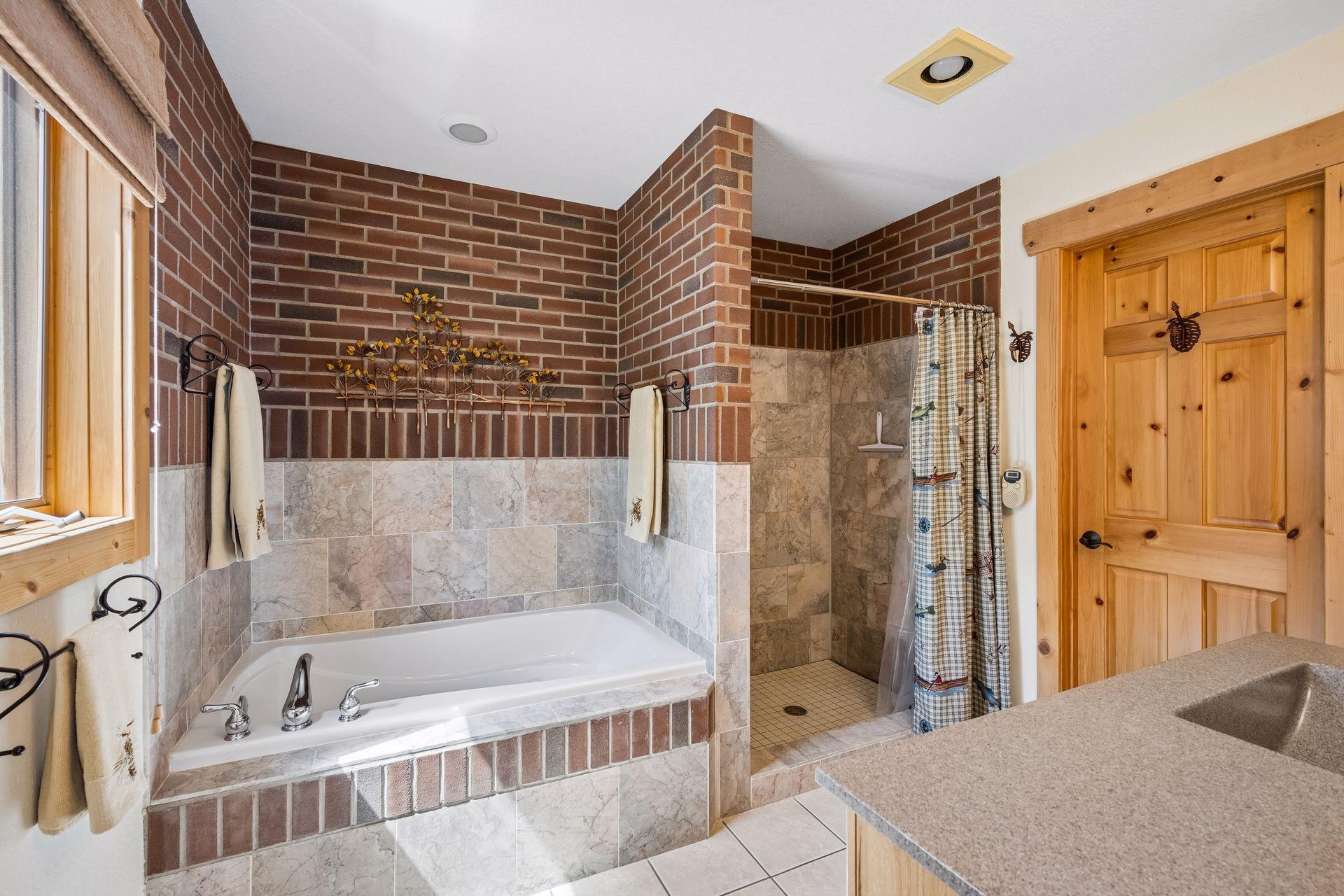 Primary suite tiled bathroom with separate tub, tile surround shower, vanity and spacious walk-in closet.