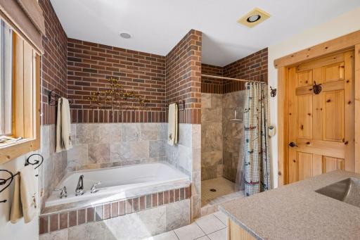 Primary suite tiled bathroom with separate tub, tile surround shower, vanity and spacious walk-in closet.