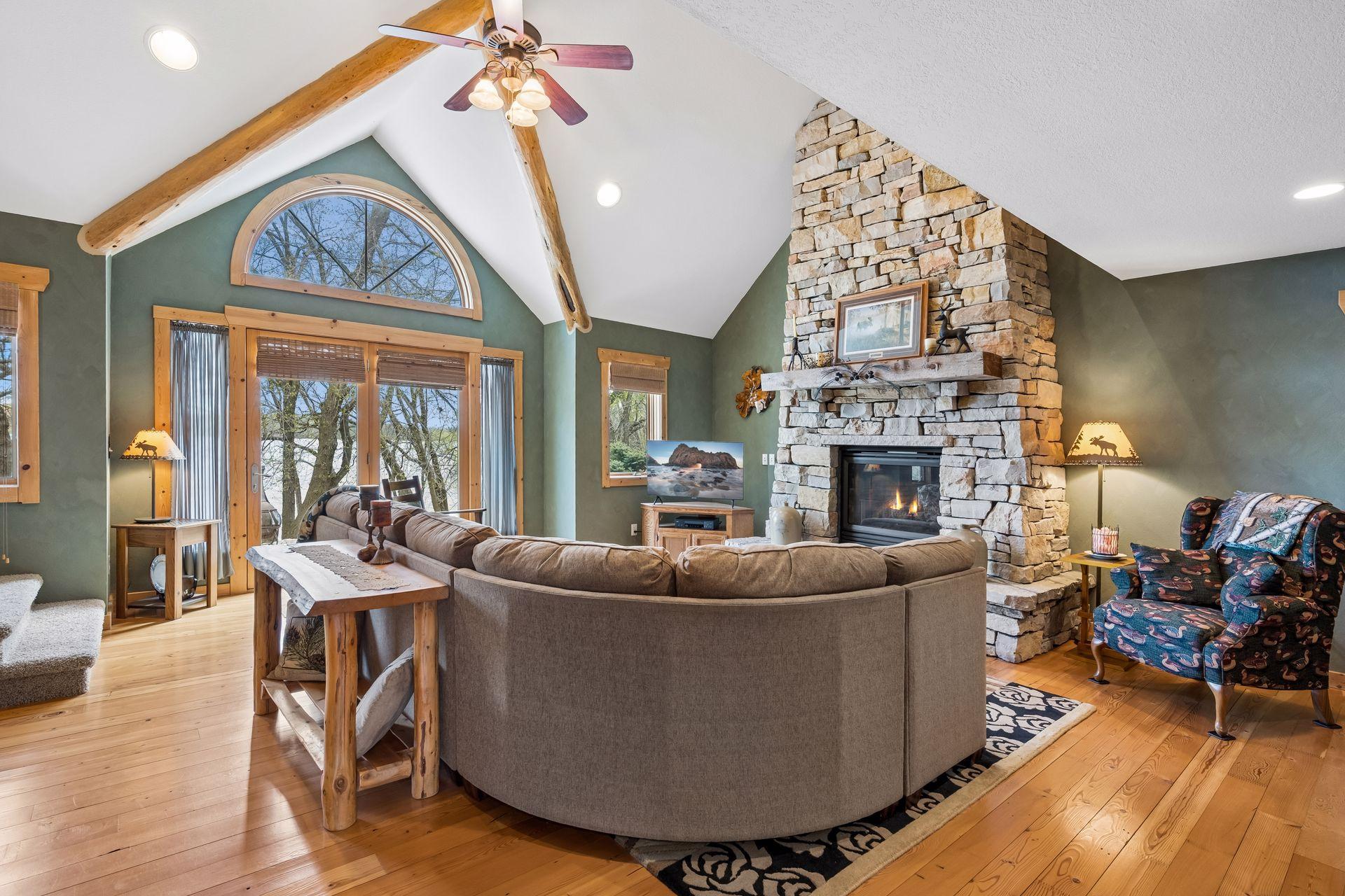 Stunning 2-story vaulted living room with soaring wood beams, floor-to-ceiling stone fireplace, and expansive lake views. Warm wood finishes and natural light create the perfect blend of cozy charm and upscale lakeside living.