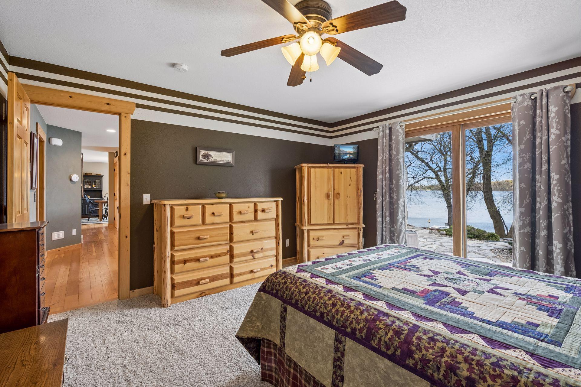 Main level primary suite featuring warm wood finishes, generous space, and expansive sliding doors showcasing serene lake views. Direct patio access enhances indoor-outdoor living, offering an inviting space to fall asleep at the end of each day.