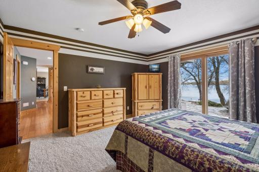 Main level primary suite featuring warm wood finishes, generous space, and expansive sliding doors showcasing serene lake views. Direct patio access enhances indoor-outdoor living, offering an inviting space to fall asleep at the end of each day.