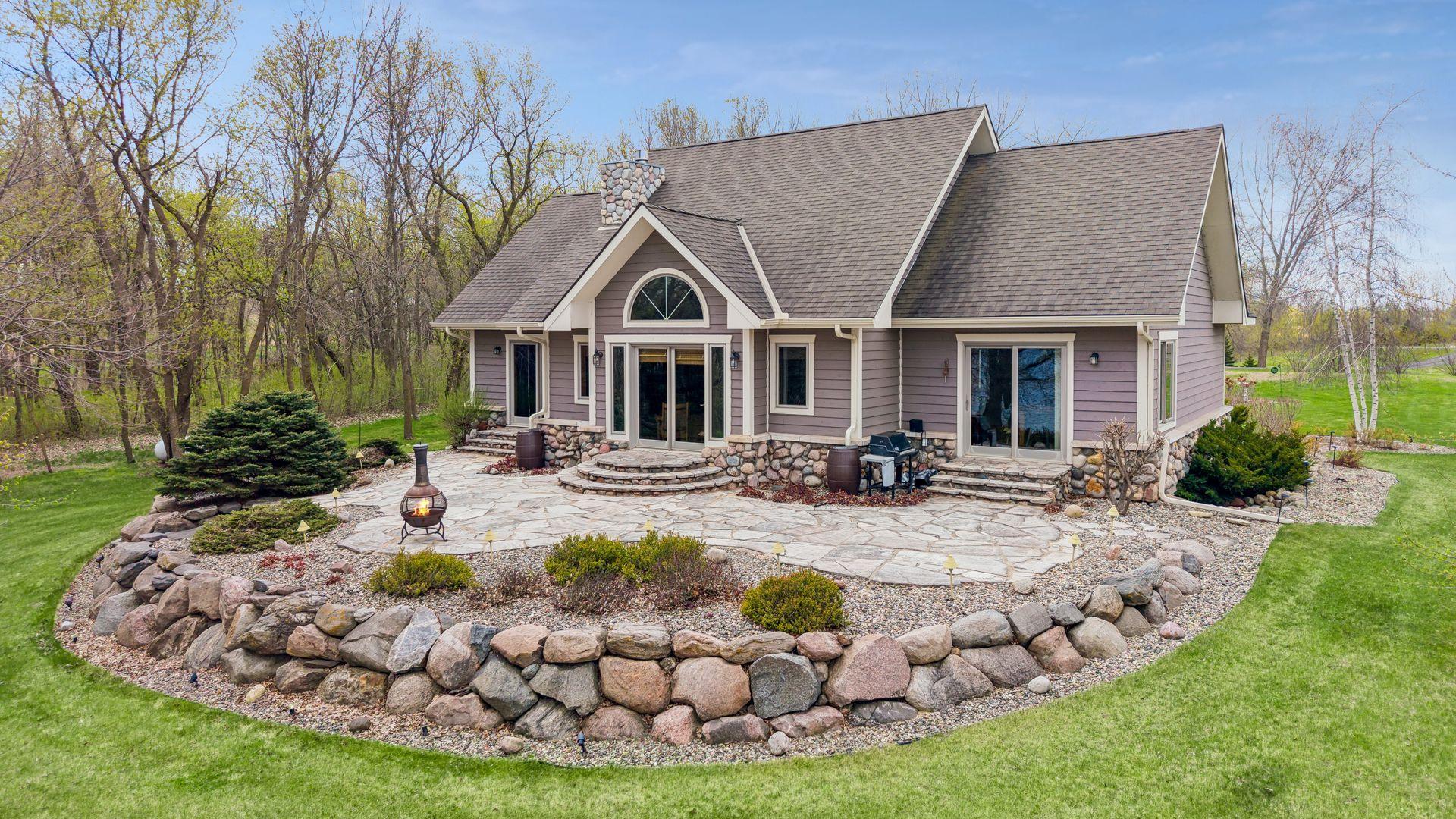 Charming lakeside home with inviting curb appeal, featuring stone accents, a spacious patio, and professional lush landscaping. Serene setting blends natural beauty creating a welcoming retreat ideal for entertaining outdoors by the lake.