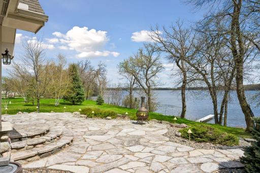 Beautiful lakeside setting on a full recreational lake in Dassel, featuring a spacious flagstone patio, mature trees, manicured lawn, and private dock. Enjoy peaceful water views, outdoor fire feature, and ideal space for relaxing or entertaining