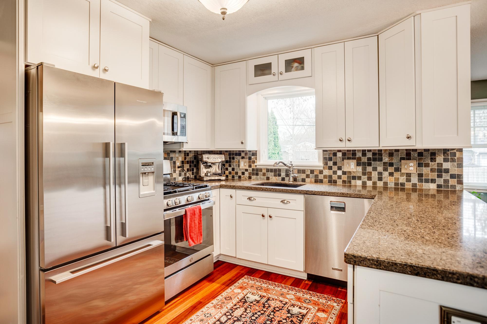 The kitchen showcases crisp, enameled cabinetry, granite countertops, stainless appliances (Fisher & Paykel fridge), and a stylish tile backsplash create a clean, timeless look.