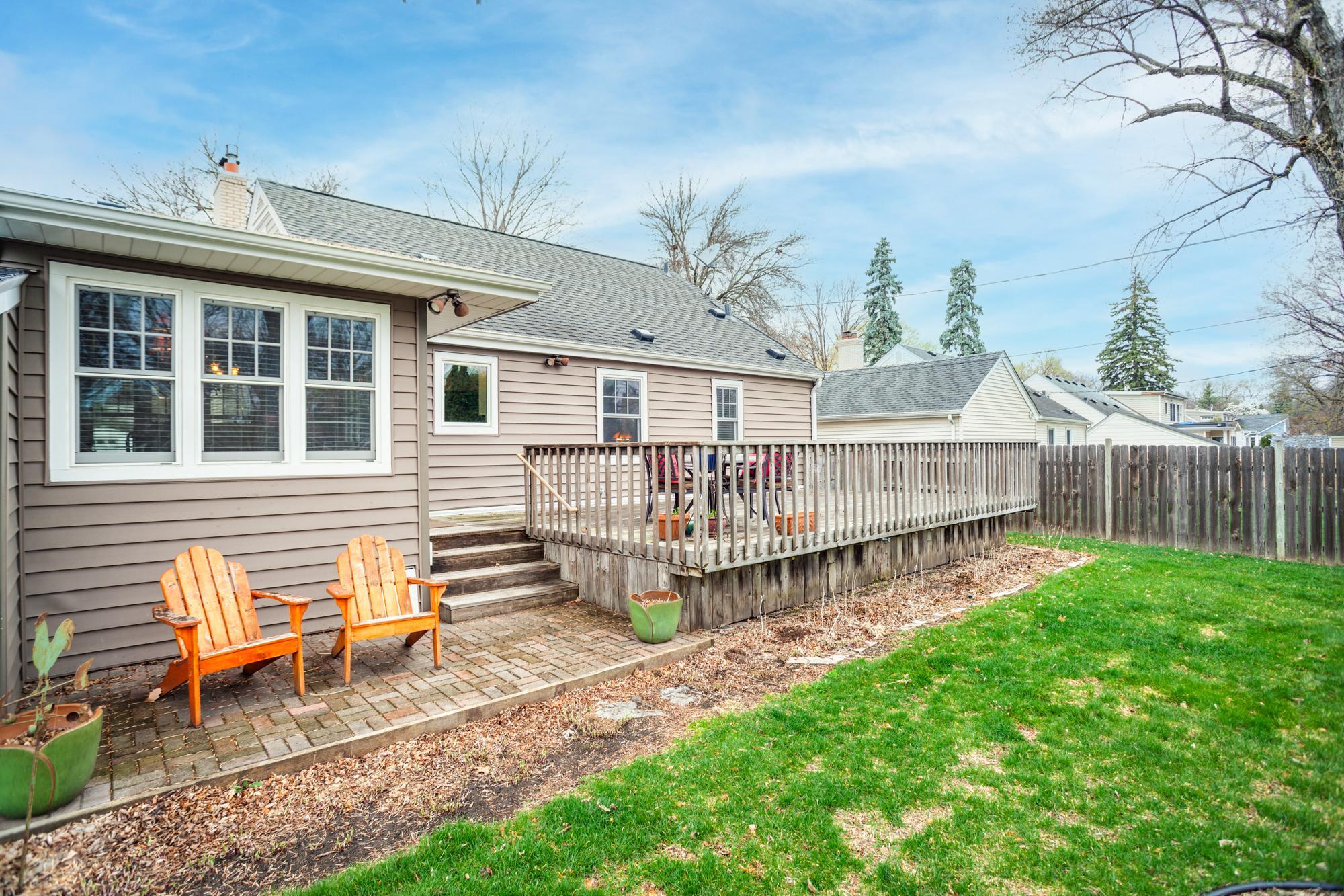 An expansive deck extends from the home and steps down to a paver patio below, creating multiple areas to relax, gather, or host guests.