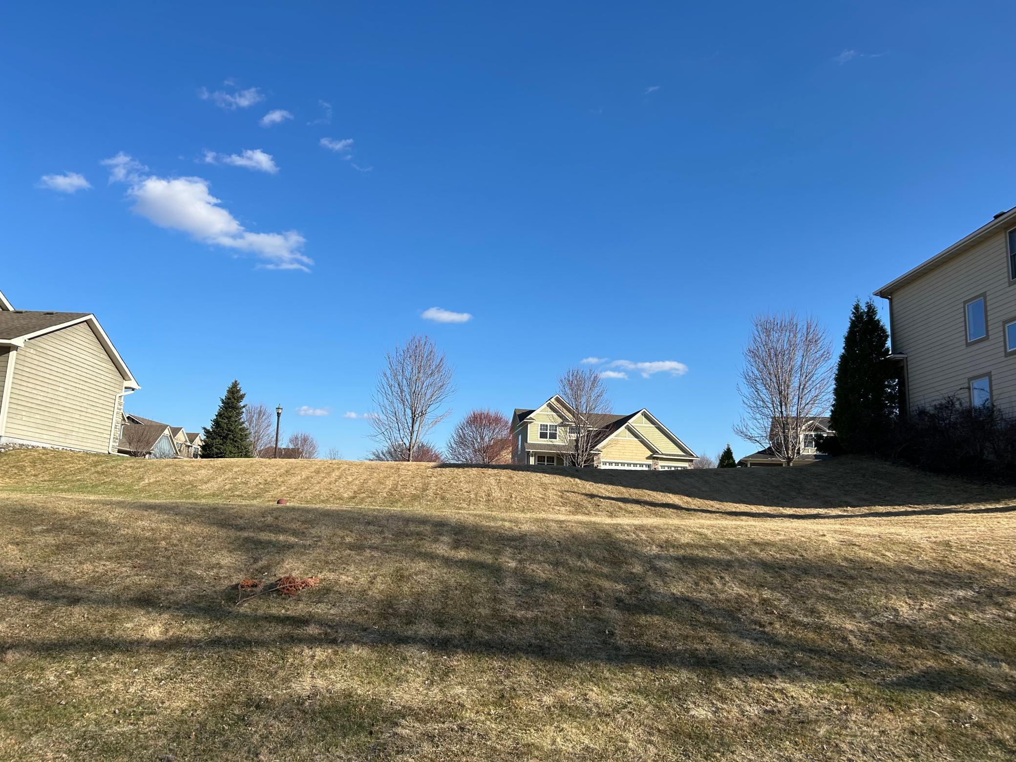 View from the water's edge looking back toward the street — see the generous lot depth and upslope topography, ideal for a walkout basement design. Quality neighboring homes in an established Cottage Grove subdivision.
