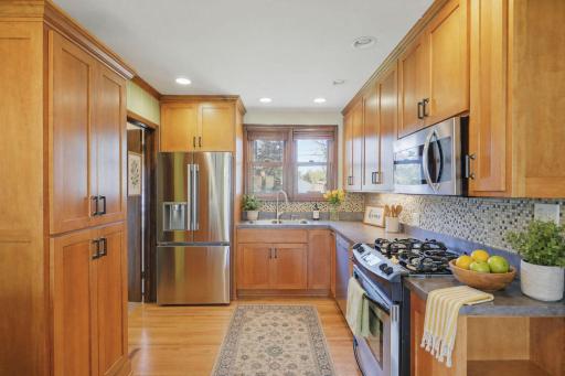 A well-equipped kitchen boasts a breakfast bar, wood cabinetry & stainless steel appliances. New french armoire style refrigerator in 2025. Kitchen was remodeled in 2020. Kitchen is virtually staged.