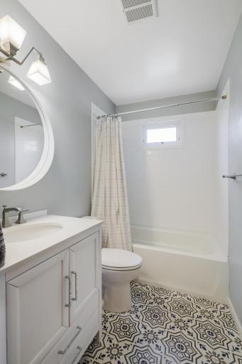 The bright and clean full bath showcases gorgeous tile flooring and cool, metal fixtures against a white backdrop. It is conveniently located on the main level between the kitchen and two bedrooms.