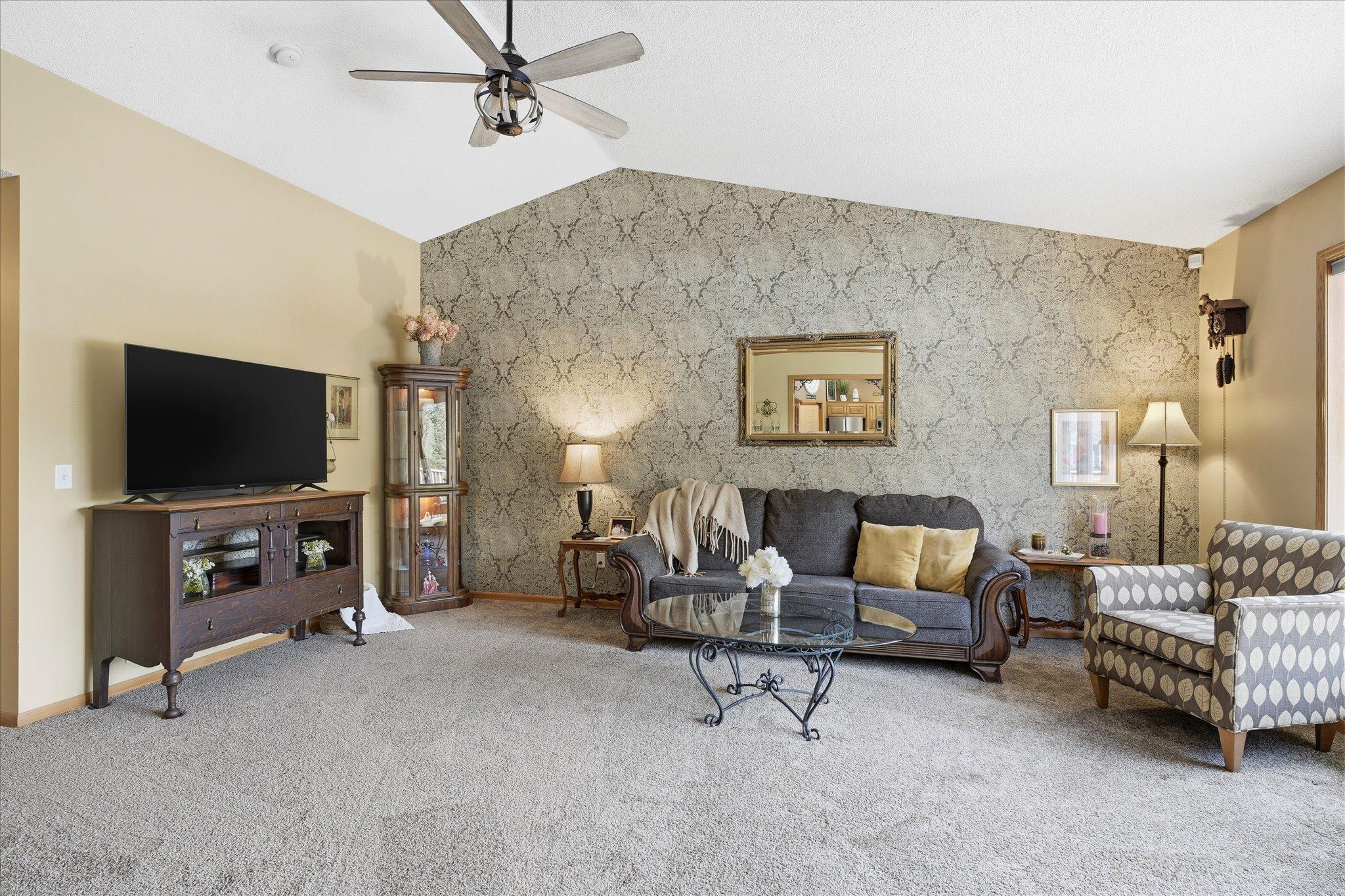 The living room has a 12' vaulted ceiling, a wallpaper accent wall and new modern & neutral carpet.