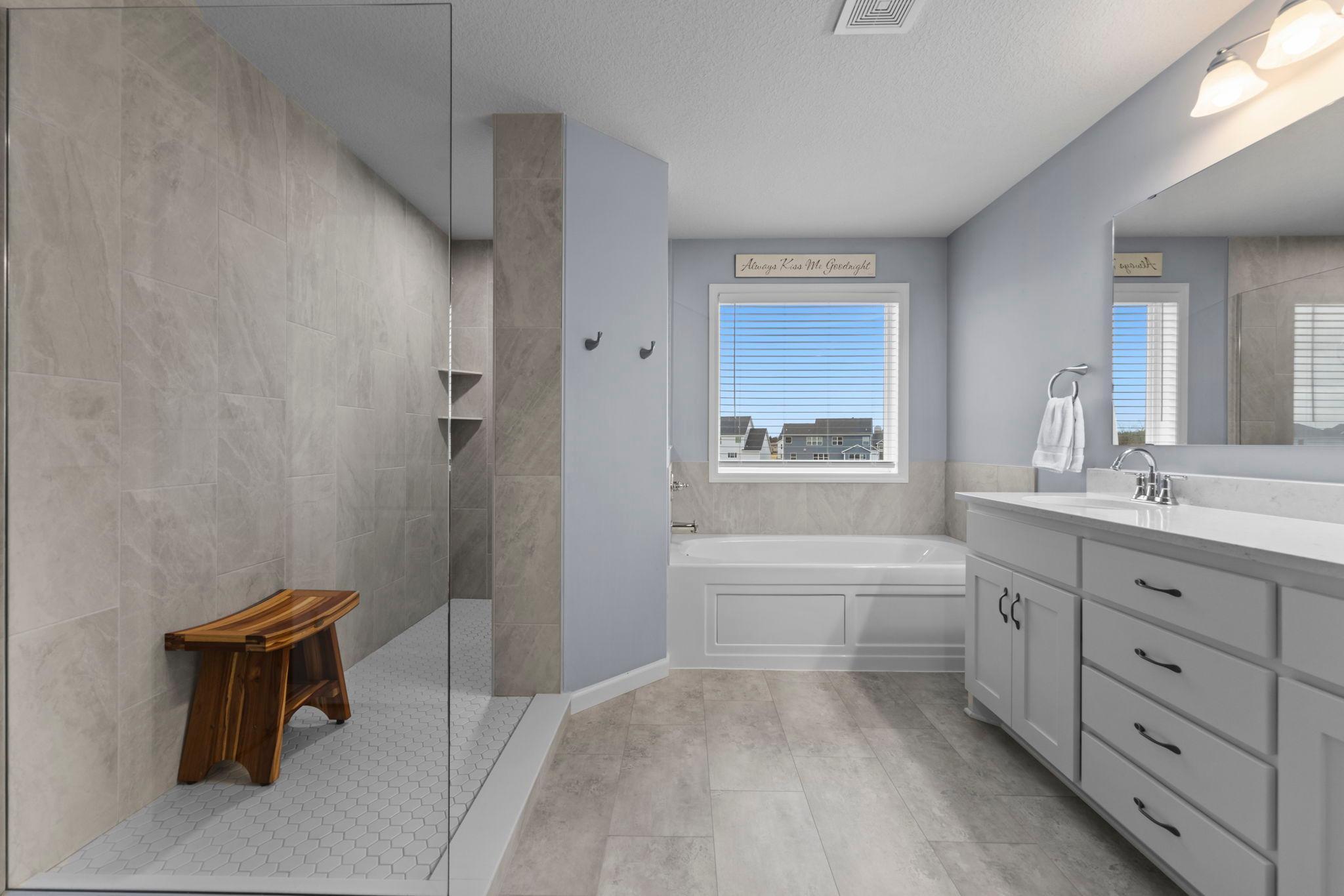 Owner's Suite Bathroom with Walk-through Shower, Soaking Tub, Window, Tinted Window, Corian Countertop, Slow Close Drawers, LVT, Built-In Shelving &Tile Surround in Shower