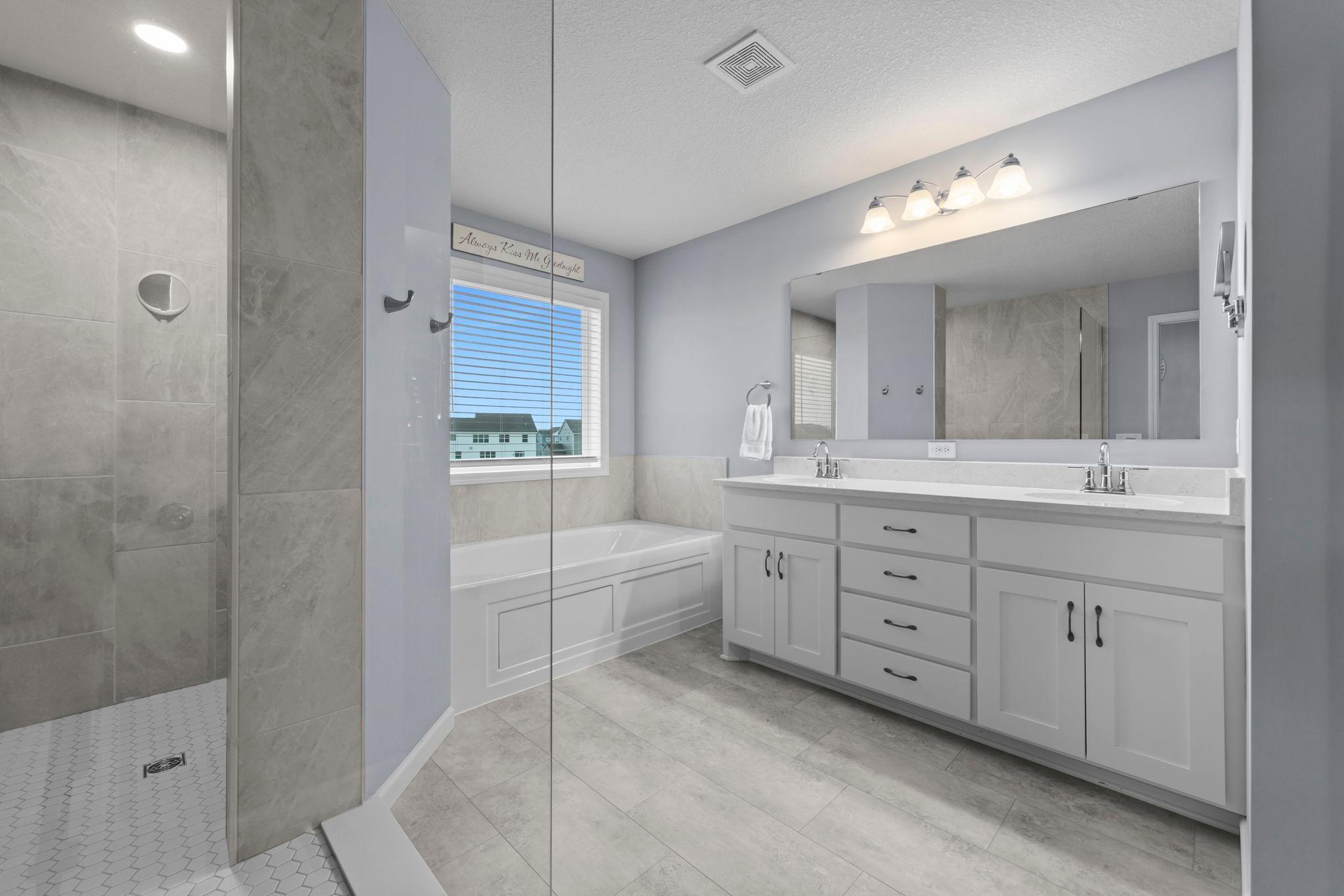 Owner's Suite Bathroom with Walk-through Shower, Soaking Tub, Window, Tinted Window, Corian Countertop, Slow Close Drawers, LVT, Built-In Shelving &Tile Surround in Shower, and Separate Toilet Room