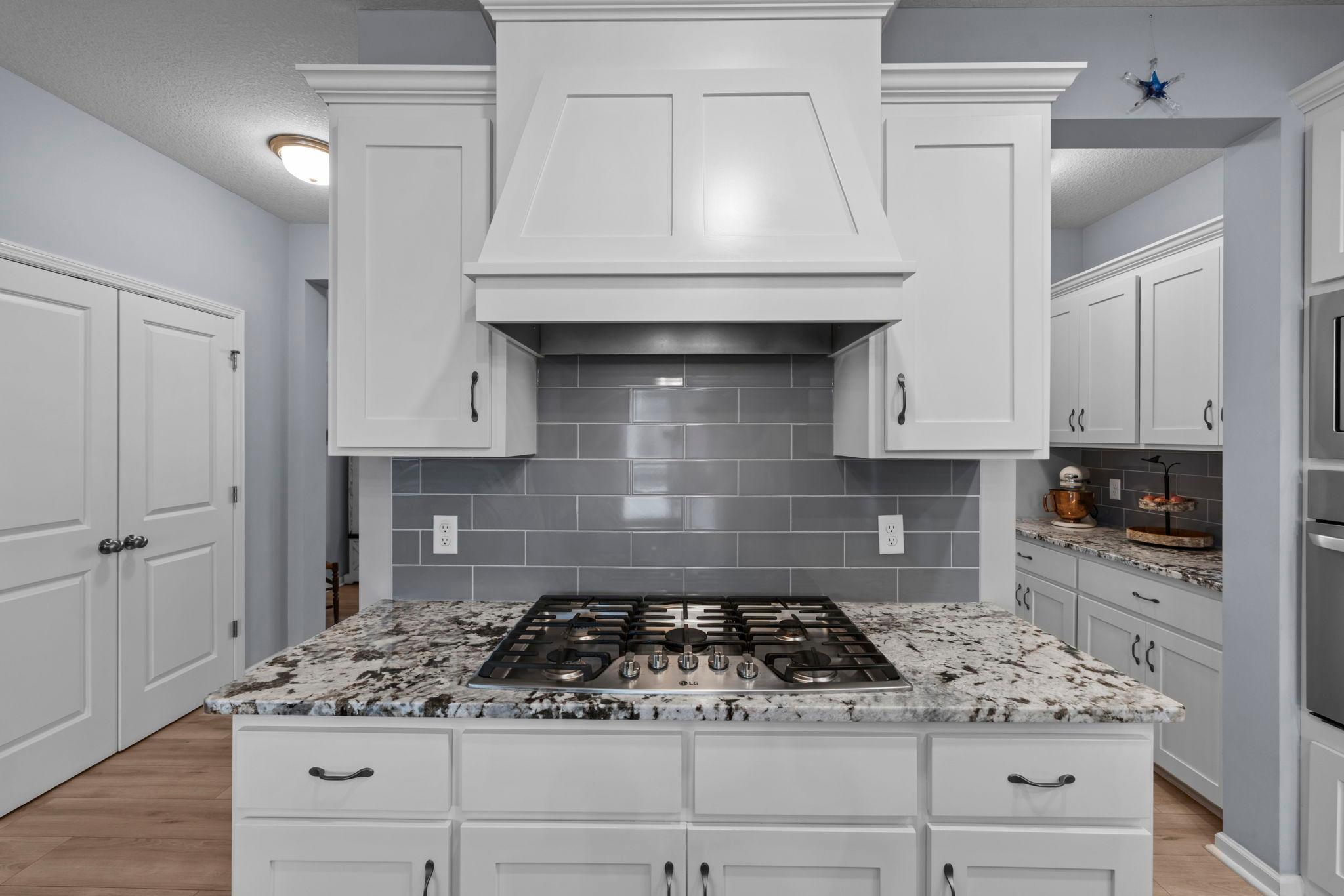 Quartz counters with cooktop, hood, tile backsplash, and slow-close drawers