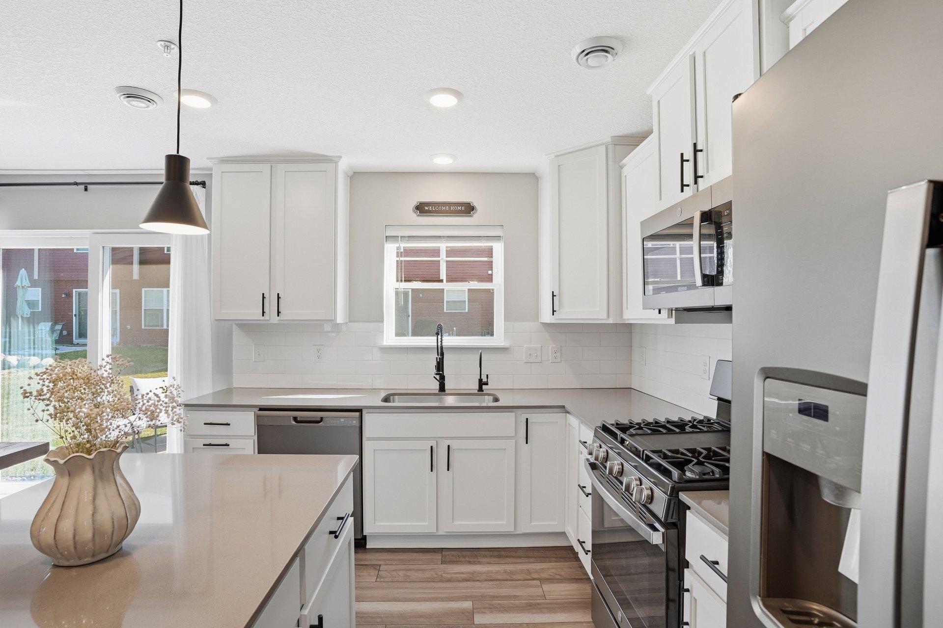 Designer kitchen with quartz countertops, slate-finish appliances, gas stove, center island, backsplash & pantry closet.