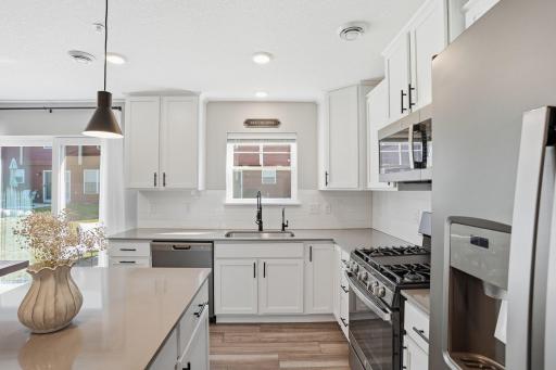 Designer kitchen with quartz countertops, slate-finish appliances, gas stove, center island, backsplash & pantry closet.