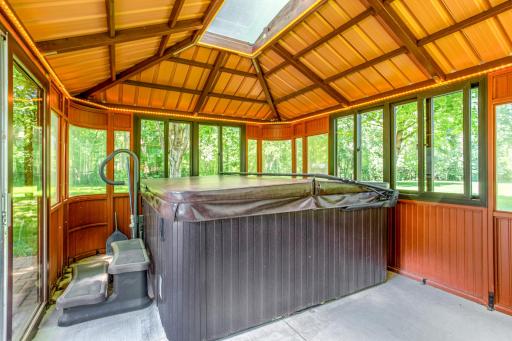 Relax and unwind year-round in the screened gazebo, featuring a private hot tub, vaulted wood-accented ceiling, and panoramic views of the surrounding mature trees and backyard.