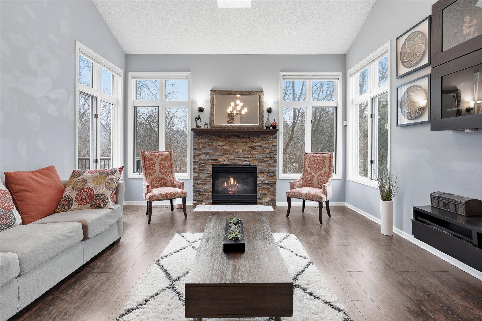 Soaring ceilings and large windows fill this great room with natural light, complemented by a cozy fireplace and elegant wood-like flooring