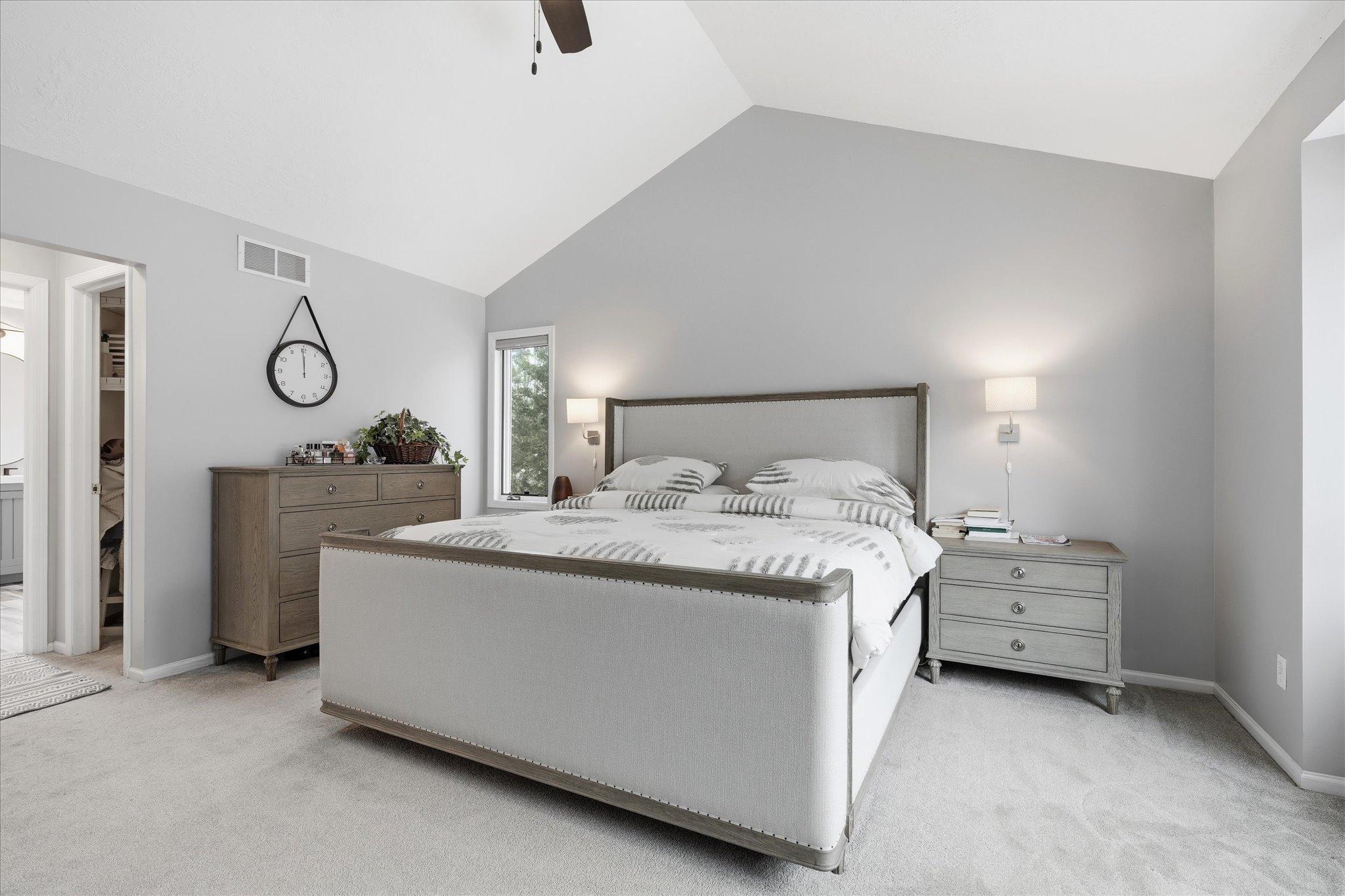 Bright and airy primary bedroom featuring vaulted ceilings, a large window with lovely views, soft neutral tones, and a walk-in closet.