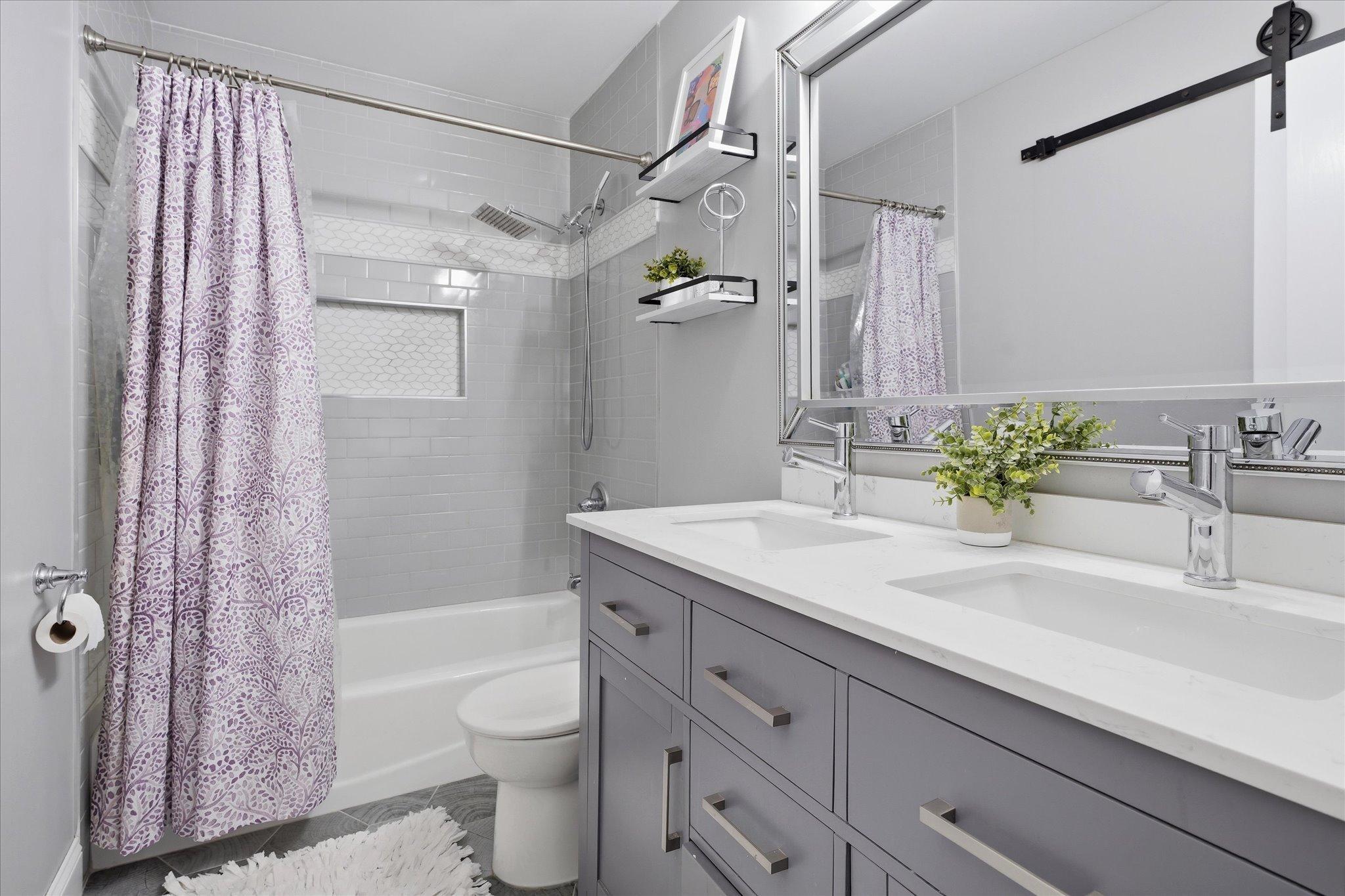 Updated full bathroom with heated tile floors, double vanity, and tile shower, offering both style and comfort.