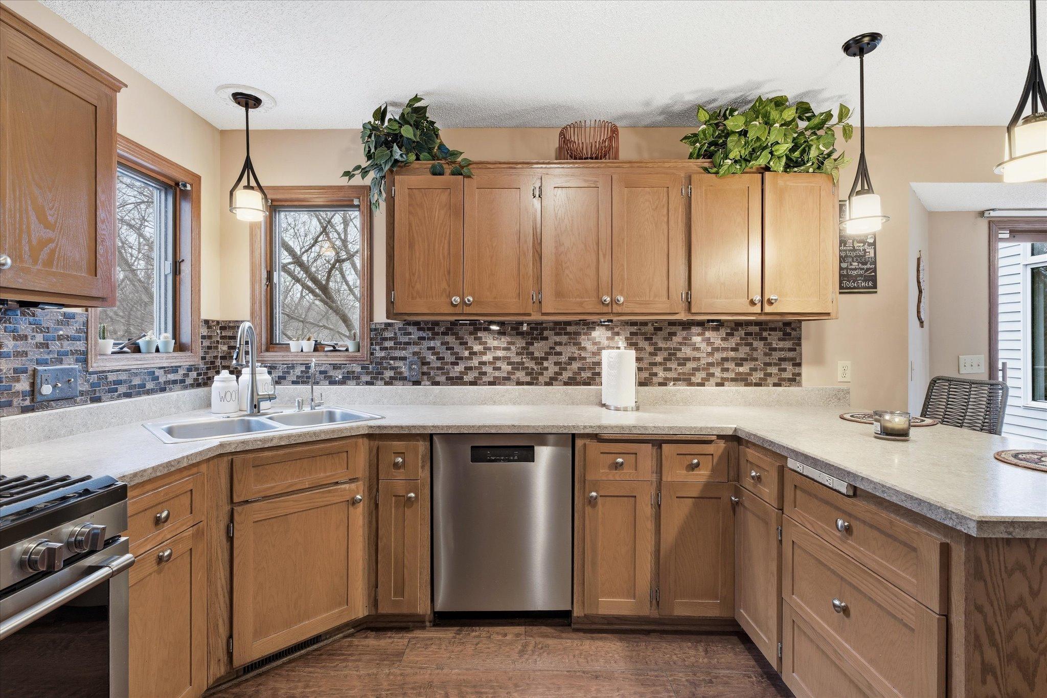 Bright kitchen with a tile backsplash, corner window above the sink, and abundant cabinetry.