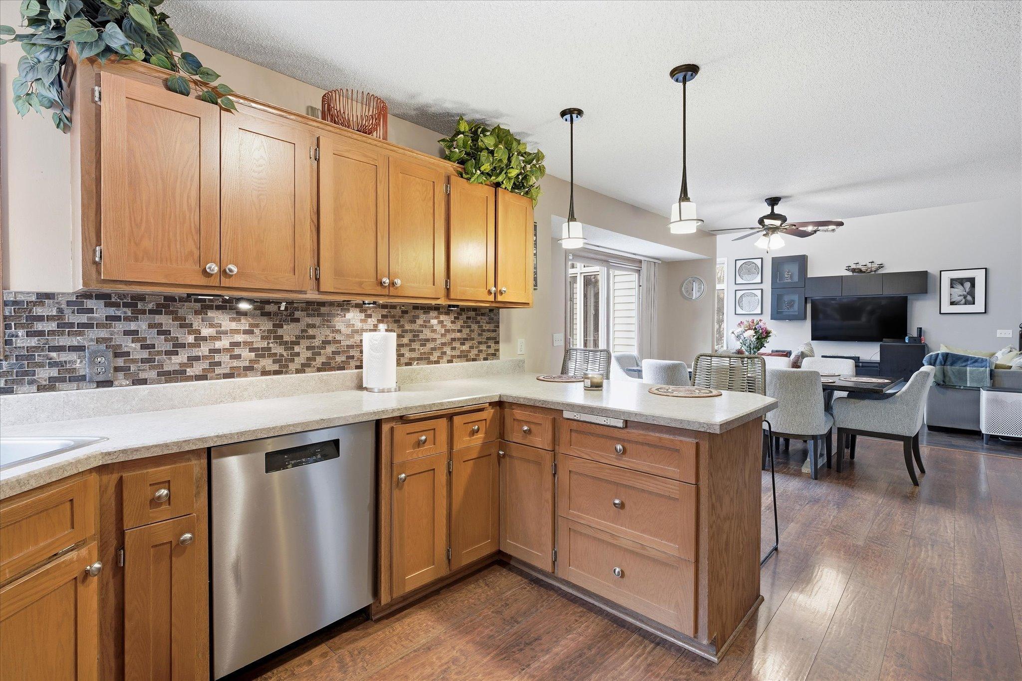 Spacious kitchen featuring ample cabinets, a charming corner window, tile backsplash, and a convenient layout connecting to the dining area.