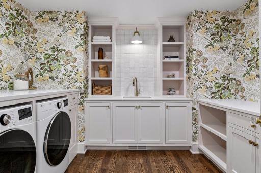 Upper level laundry room features custom wallpaper, utility sink with built ins and large folding area