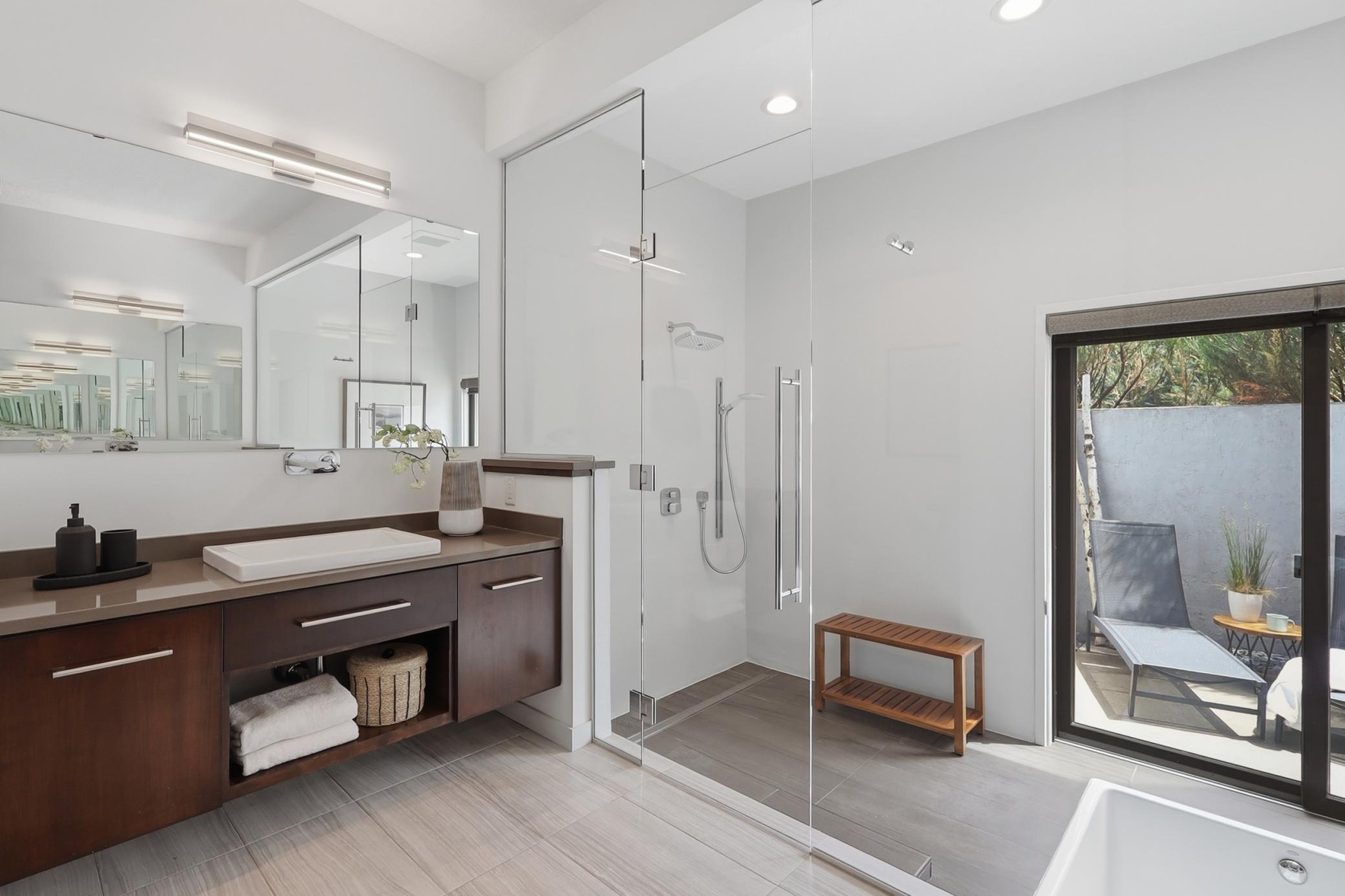 This en suite bath was perfectly designed with spa vibes, two separate vanities, a full-on wet room enclosed in floor to ceiling glass. The walk-in soaker tub leads out onto a private patio enclosure!